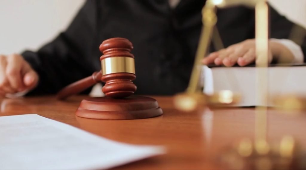 A judge's gavel on a desk, with scales of justice and legal documents behind it