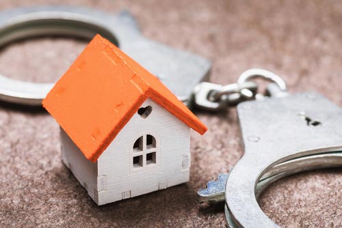 Miniature house with an orange roof next to a pair of handcuffs